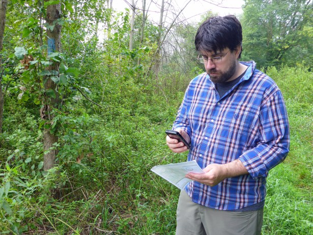 Matt Rowbotham, the cartographer for the North Country Trail Association, stops along the trail (marked by blue blazes on trees) to compare information on a paper map and the new digital map for the trail. Photo by Howard Meyerson